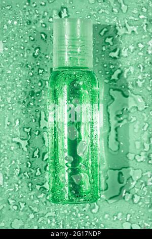 Piccola bottiglia trasparente con gocce d'acqua su sfondo verde, vista dall'alto Foto Stock