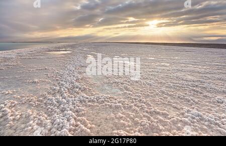 Spiaggia cristallina di sale bianco illuminata dal sole del mattino, piccole pozzanghere con acqua di mare al Mar Morto - il lago più iperialino del mondo Foto Stock