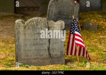 Primo piano di un'antica pietra tomba con una bandiera americana accanto ad essa al Granary Burying Ground a Boston Foto Stock