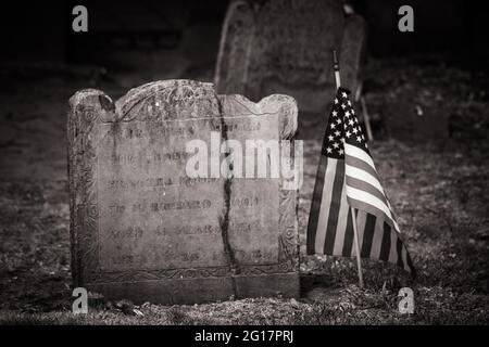 Primo piano di un'antica pietra tomba con una bandiera americana accanto ad essa al Granary Burying Ground a Boston Foto Stock