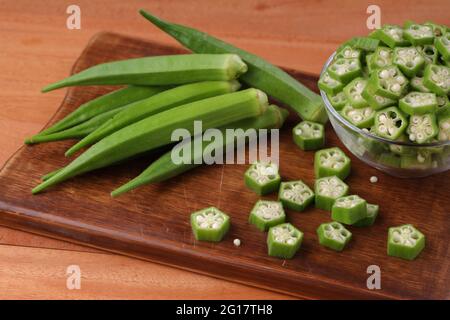 Okra o il dito della signora o Bhindi verdure fresche verdi disposte su un tagliere con alcuni anelli tagliati messi in una ciotola di vetro, fuoco selettivo. Foto Stock