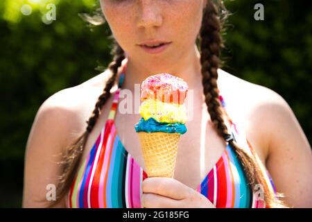 Giovane ragazza adolescente che mangia cono di icecream con occhiali da sole rosa e trecce nel caldo giorno d'estate Foto Stock