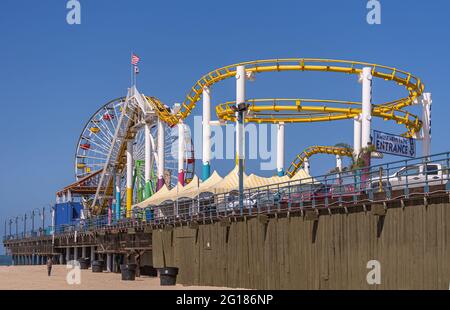 Santa Monica, CA, USA - 20 giugno 2013: Traghetti permanenti colorati ruote e montagne russe sul molo. Sparato lungo il molo dalla sabbia sotto il cielo blu. Foto Stock