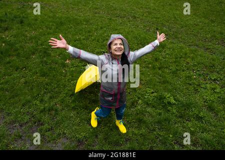 Donna anziana felice, matura allegra, anziana, donna in pensione con ombrello giallo godendo la vita in una giornata piovosa nel parco. Goditi ogni momento, godendoti la vita Foto Stock