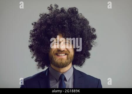 Studio ritratto di felice uomo d'affari in costume e pazzo parrucca ricciolo sorridente a macchina fotografica Foto Stock