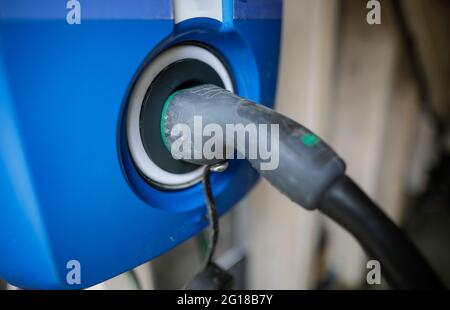 Immagine della profondità di campo ridotta (messa a fuoco selettiva) con un cavo di ricarica per auto elettrica e una presa su una stazione di ricarica. Foto Stock