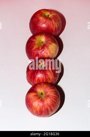 Colpo verticale di mele rosse mature in fila su una superficie bianca Foto Stock