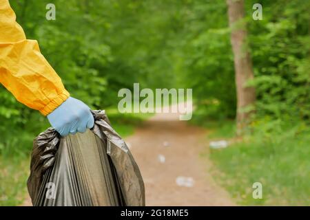 Volontariato pulizia di rifiuti un parco. La gente cura terra inquinamento plastica spazzatura lavoratore mano che tiene sacchetto di spazzatura. Mani di volontariato raccoglie una plastica Foto Stock