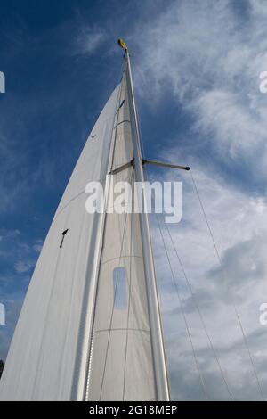 Guardando l'albero di metallo di una barca a vela sotto la vela. Uno yacht di bermuda rigged, con una grande vela bianca contro un bel cielo blu con nuvole bianche Foto Stock
