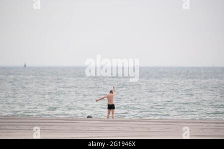 06 giugno 2021, Schleswig-Holstein, Travemünde: Un uomo si riscalda sulla spiaggia prima di nuotare nel Mar Baltico. Foto: Daniel Reinhardt/dpa Foto Stock