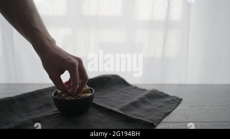 Uomo Pick pistacchi salati da ciotola nera su tavola di quercia, foto ampia Foto Stock