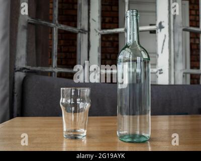 Bottiglia di vetro trasparente con acqua o vino bianco e due bicchieri di vetro vuoti. Foto Stock