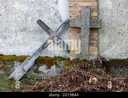 Una vecchia croce appoggiata contro un muro in un cimitero Foto Stock