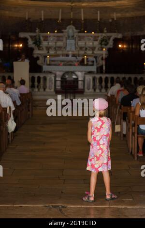 Giovane ragazza che osserva il servizio domenicale alle soglie di una chiesa di Bonifacio. Corsica, Francia Foto Stock