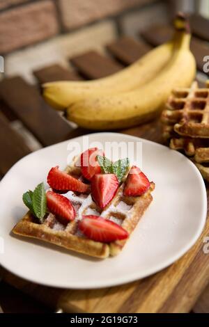 Vista della colazione, waffle belgi con fragola e banana con menta su sfondo di legno Foto Stock