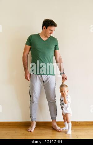 Il papà sorridente tiene la mano di un piccolo bambino in piedi sul pavimento nella stanza Foto Stock