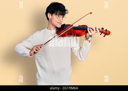 Bell'hipster giovane uomo che suona violino sorridendo guardando al lato e fissando via pensare. Foto Stock