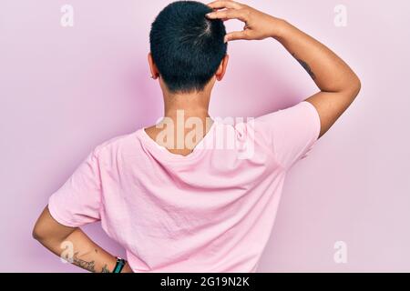 Bella donna ispanica con capelli corti indossando casual t shirt rosa all'indietro pensando al dubbio con la mano sulla testa Foto Stock