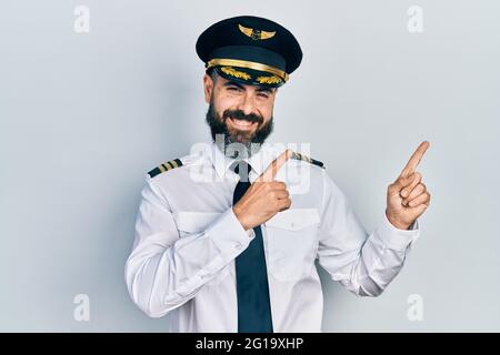 Giovane uomo ispanico che indossa l'uniforme di pilota di aeroplano sorridente e guardando la macchina fotografica che punta con due mani e le dita a lato. Foto Stock