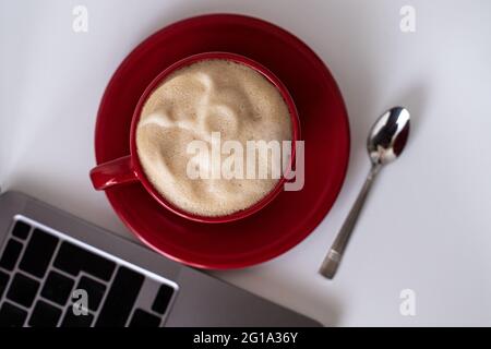 Scrivania da ufficio a piano. Tazza rossa con vista dall'alto. Lavora da casa. scrivania con computer portatile e tazza di caffè su un tavolo bianco. Copia della vista superiore piatta Foto Stock