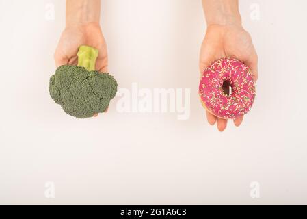 Confronto delle abitudini alimentari. Donna che tiene broccoli e ciambella su sfondo bianco Foto Stock