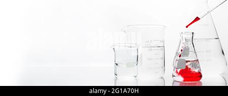 matraccio e becher in vetro trasparente con soluzione di goccia arancione in fondo banner bianco per laboratori di ricerca chimica scientifica Foto Stock