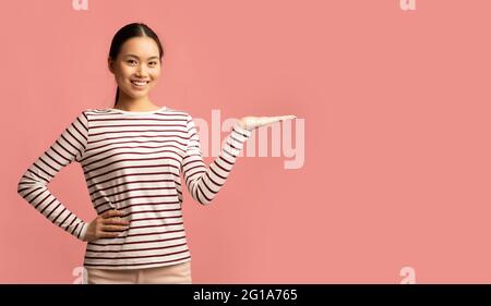 Controllare. Donna asiatica positiva che tiene qualcosa sulla sua palma vuota aperta Foto Stock