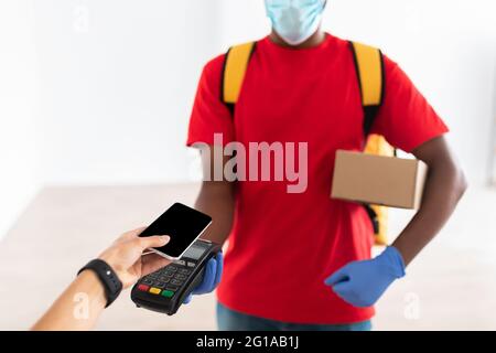 Uomo nero che tiene il cliente della macchina del POS che paga con lo smartphone Foto Stock