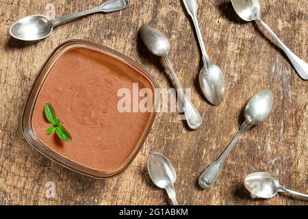 Una ciotola con mousse di cioccolato francese tradizionale con una foglia di menta e molti cucchiai sul vecchio sfondo di legno, vista dall'alto Foto Stock