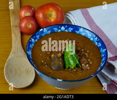 Zuppa di lenticchie fatta in casa con salsicce di maiale chiamato chorizo, salsiccia di sangue chiamato Morcilla e pepe verde in una ciotola decorata con pomodori, un cucchiaio e. Foto Stock