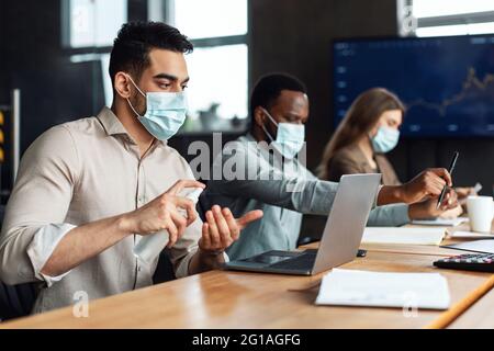 Colleghi internazionali che indossano maschere mediche utilizzando igienizzatore sulle mani Foto Stock