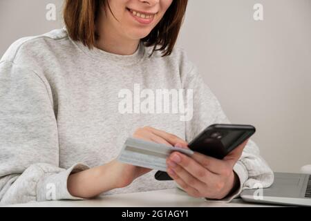 Felice donna sorridente che tiene la carta di credito e paga tramite telefono cellulare. Il cliente effettua gli acquisti online e riceve il rimborso. Foto Stock
