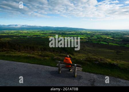 Un uomo si siede su una panchina vicino al bordo della strada ammirando il panorama al Vee Pass, una curva a forma di V sulla strada Foto Stock