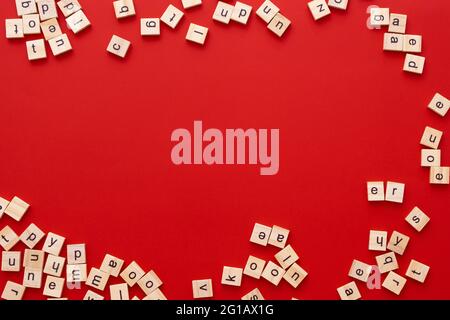 Immagine di sfondo le lettere sono sparse in disordine. Lettere inglesi. Lettere quadrate di legno su sfondo rosso brillante. Biglietto d'auguri, pronto all'uso Foto Stock