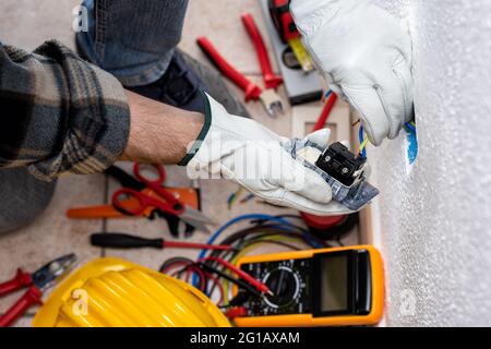 Vista dall'alto. L'elettricista inserisce i cavi elettrici nei terminali della presa di un impianto elettrico. Lavorare in sicurezza con i guanti di protezione. Foto Stock