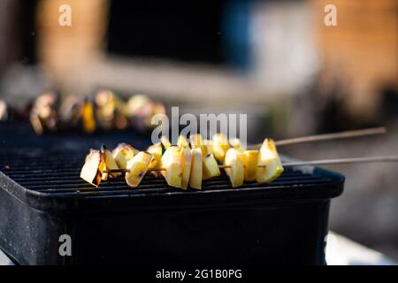 Un barbecue estivo all'aperto con fette di patate arrostite su una griglia per riunirsi con le famiglie durante le vacanze Foto Stock