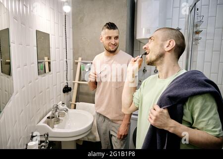 Due giovani gay spazzolando i denti in bagno la mattina Foto Stock