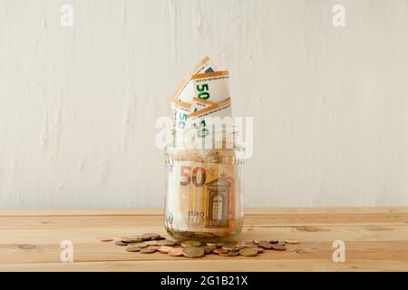 banconote in euro nel vaso di vetro a tavola di legno con monete in euro o centesimi. Concetto aziendale. Risparmio di denaro in pentola di vetro a casa. Foto Stock