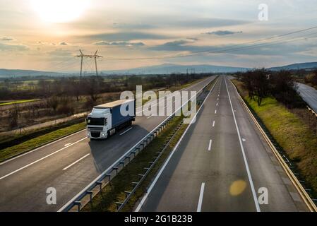 Camion con semi-rimorchio che guida lungo l'autostrada sullo sfondo del cielo del tramonto. Consegna merci su strada. Servizi e logistica dei trasporti Foto Stock