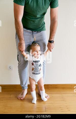 La bambina si alza e tiene le mani del papà nella stanza Foto Stock