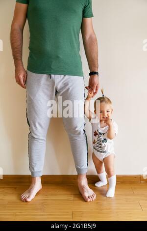 Papà tiene la mano di un piccolo bambino con una coda di pony in piedi sul pavimento nella stanza Foto Stock