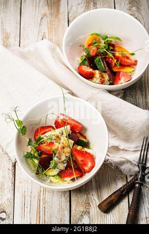 Vista dall'alto, deliziosa insalata estiva. Insalata con fragole fresche, barbabietole da forno, pomodori gialli, formaggio blu dor ed erbe aromatiche in un recipiente bianco Foto Stock