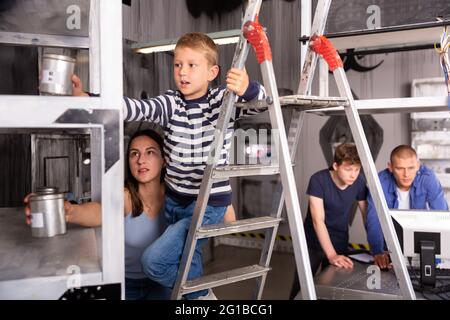 Presteen ragazzo con mamma che cerca di raggiungere per la lattina nella stanza di ricerca Foto Stock