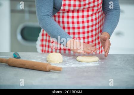 Una donna piuttosto matura stira fuori l'impasto scolpito con un mattarello in cucina sul tavolo. Nonna casalinga. Foto Stock