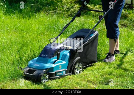 Donna che taglia l'erba utilizzando il rasaerba elettrico, vista ravvicinata. Foto Stock