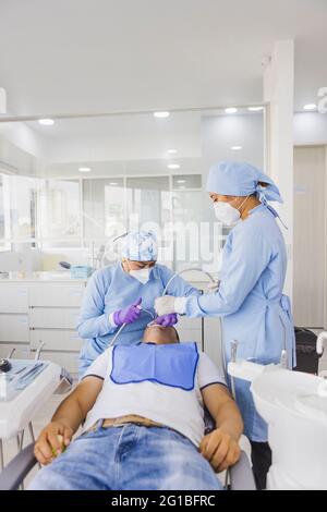 Stomatologa femminile che cura i denti di un paziente maschile irriconoscibile contro il collaboratore in uniforme in ospedale Foto Stock