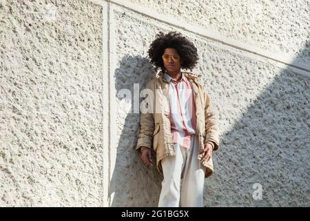 Serious African American maschio in outfit elegante che cavalcano moderno elettrico scooter lungo la strada e guardando la macchina fotografica Foto Stock