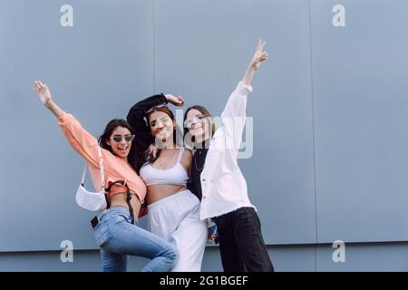 Amici femminili positivi in occhiali da sole alla moda e vestiti casual che ridono felice mentre trascorrono il tempo piacevole insieme Foto Stock