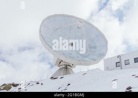 Dal basso dell'antenna satellitare sulla montagna innevata contro la facciata dell'edificio sotto il cielo nuvoloso in Spagna Foto Stock