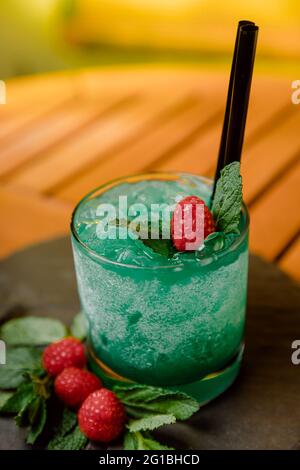 Alto angolo di cocktail esotico fatto di gin con frutto della passione mescolato con succo di limone e curacao blu servito con frutti di bosco e foglie di menta Foto Stock
